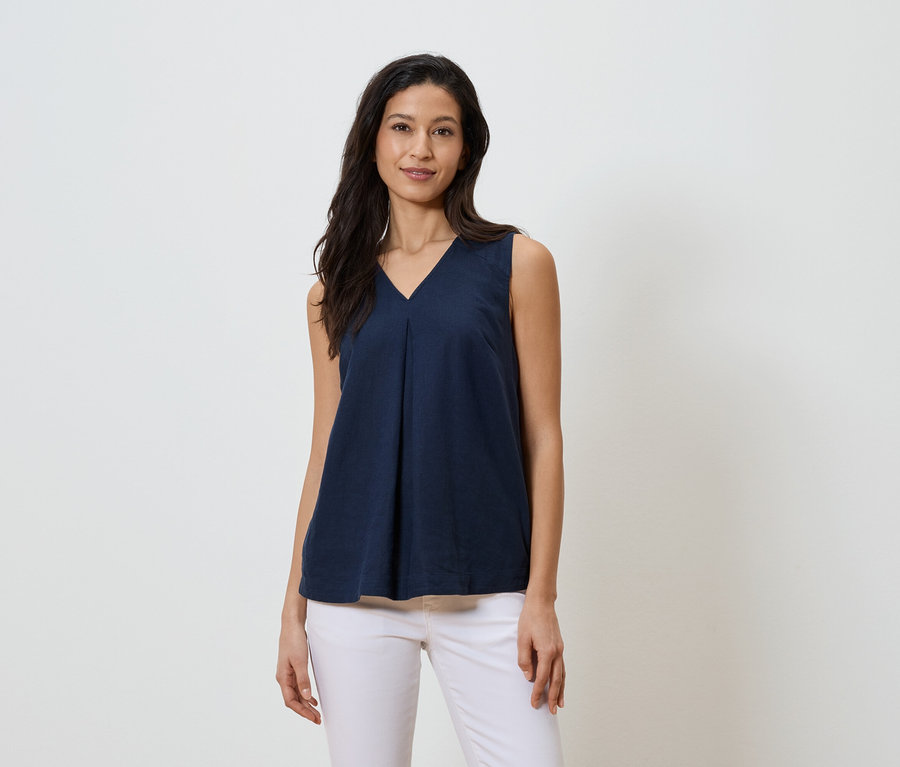 Une femme porte un haut bleu marine sans manches à col en V et un jean blanc.