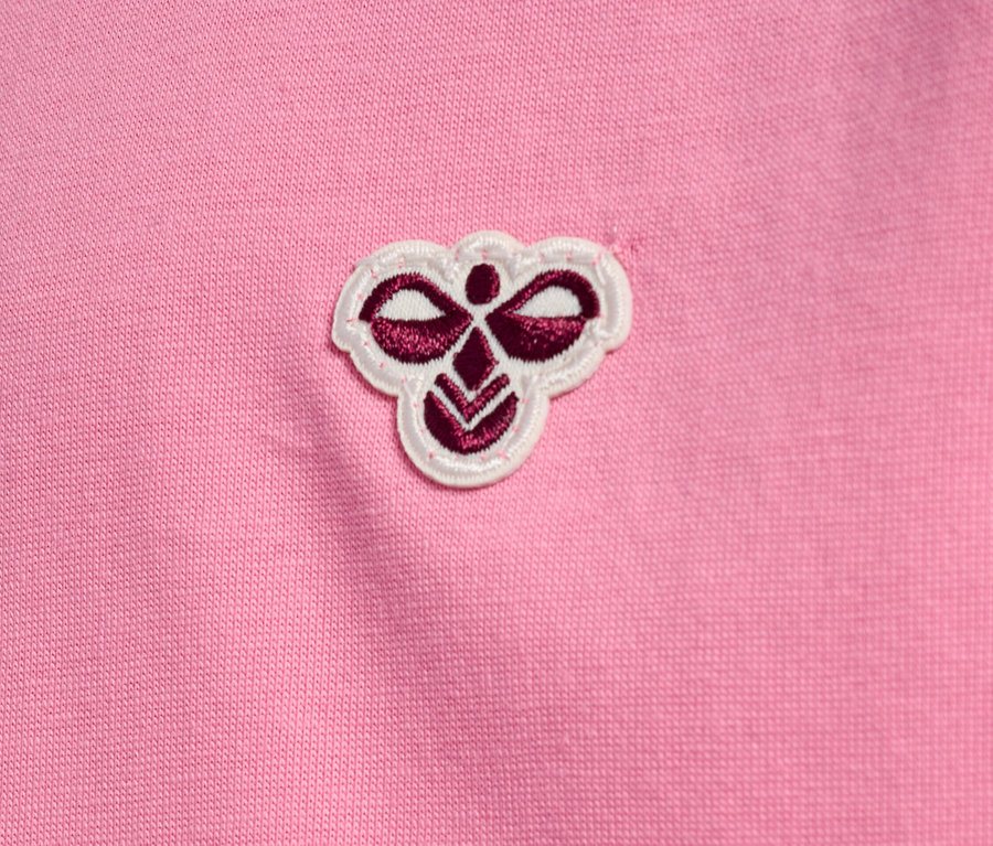 Gros plan d'un tissu rose avec un petit logo brodé en haut au centre.