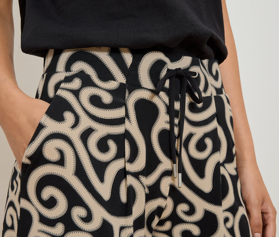 Femme avec une main dans la poche d'un pantalon à motif tourbillonnant noir et beige avec cordon de serrage.