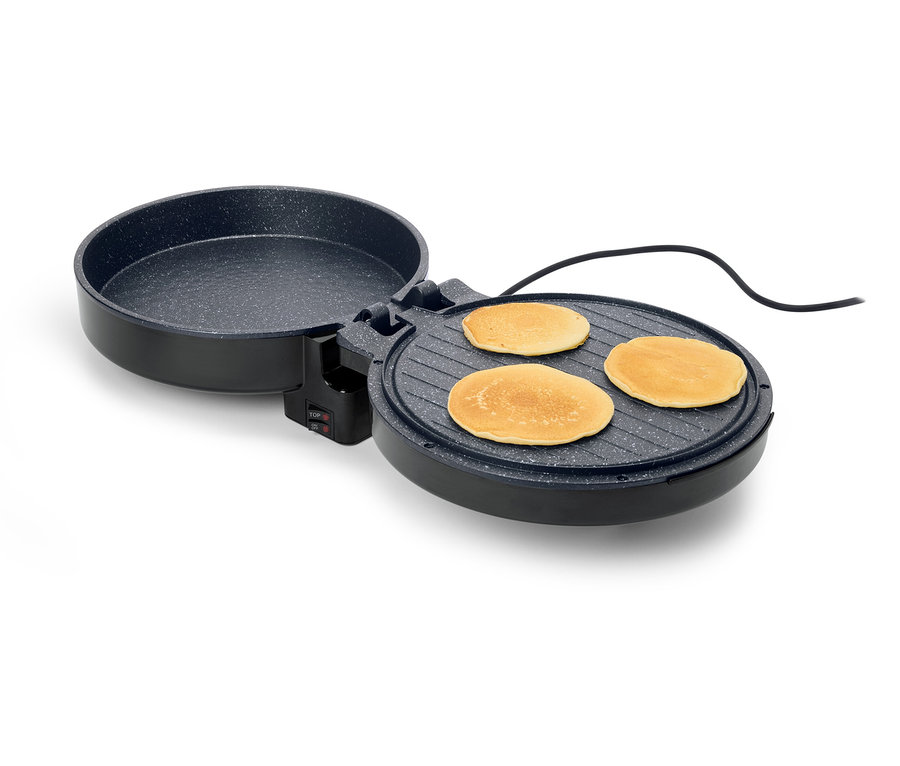 Une crêpière noire, ronde et ouverte avec trois crêpes dessus, sur un fond blanc.