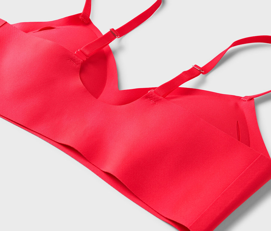 Gros plan d'un soutien-gorge rouge avec des bretelles réglables sur un fond gris clair.