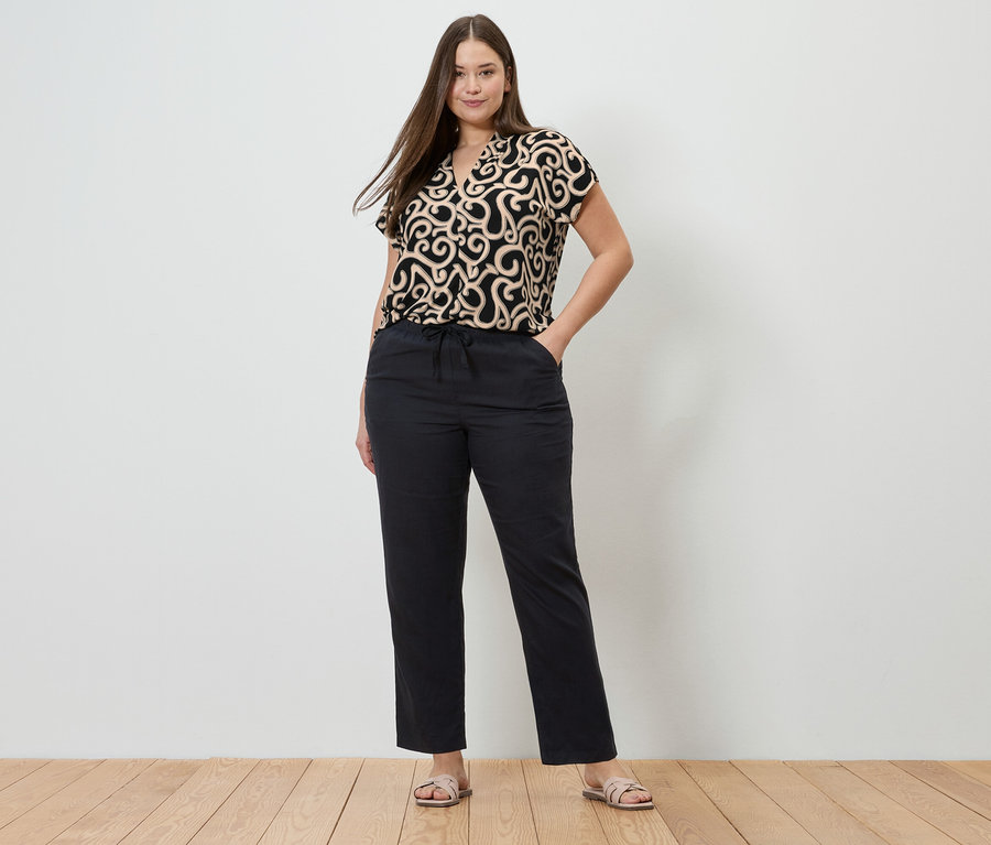 Femme portant un haut à motifs et un pantalon en lin noir. Le pantalon en lin est noir.