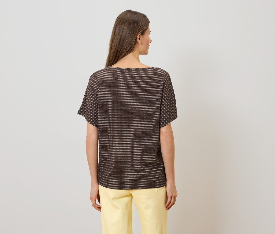 Vue arrière d'une femme aux cheveux bruns portant un haut rayé marron et un pantalon jaune.