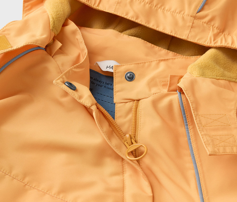 Gros plan d'une veste orange à capuche avec doublure en polaire jaune, fermeture éclair et boutons-pression.