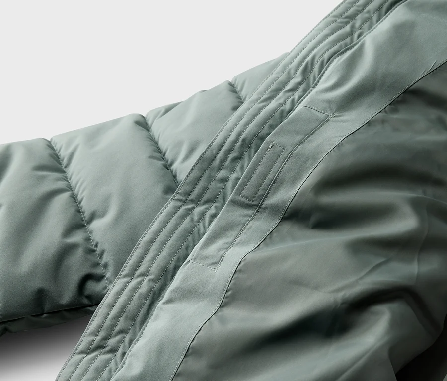 Gros plan d'un manteau matelassé vert clair avec une couture le long de l'épaule.