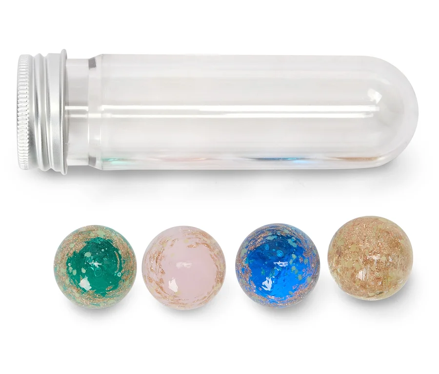 Un tube à essai transparent avec un bouchon à vis argenté est posé horizontalement au-dessus de quatre sphères mouchetées et pailletées. Les sphères sont vertes, roses, bleues et beiges, alignées sous le tube.