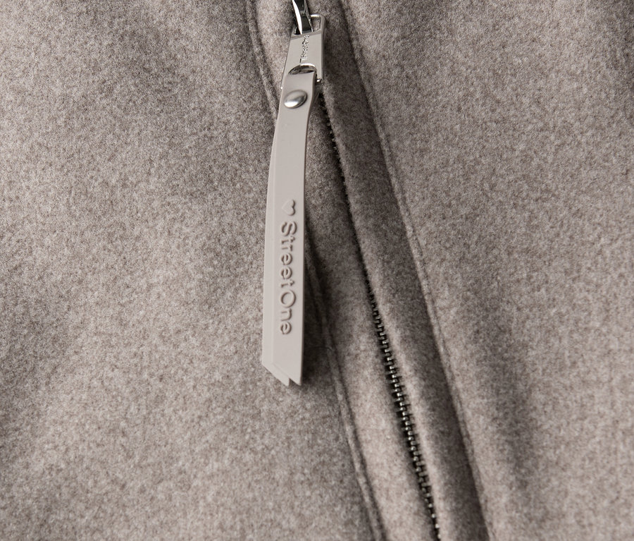 Gros plan sur un manteau court Street One avec fermeture éclair et pendentif.