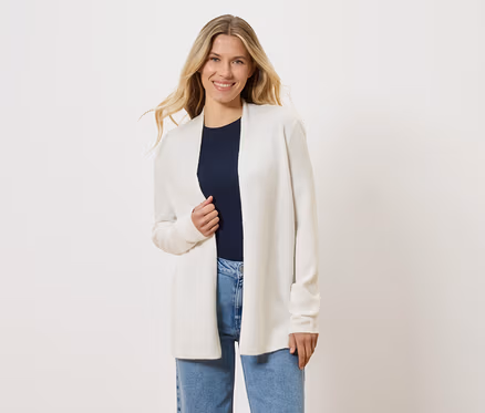 Une femme blonde porte un cardigan ouvert blanc sur un t-shirt bleu marine et un jean bleu.