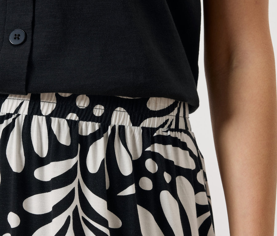 Gros plan d'une personne portant un haut noir boutonné et une jupe à motif de feuilles noires et blanches.