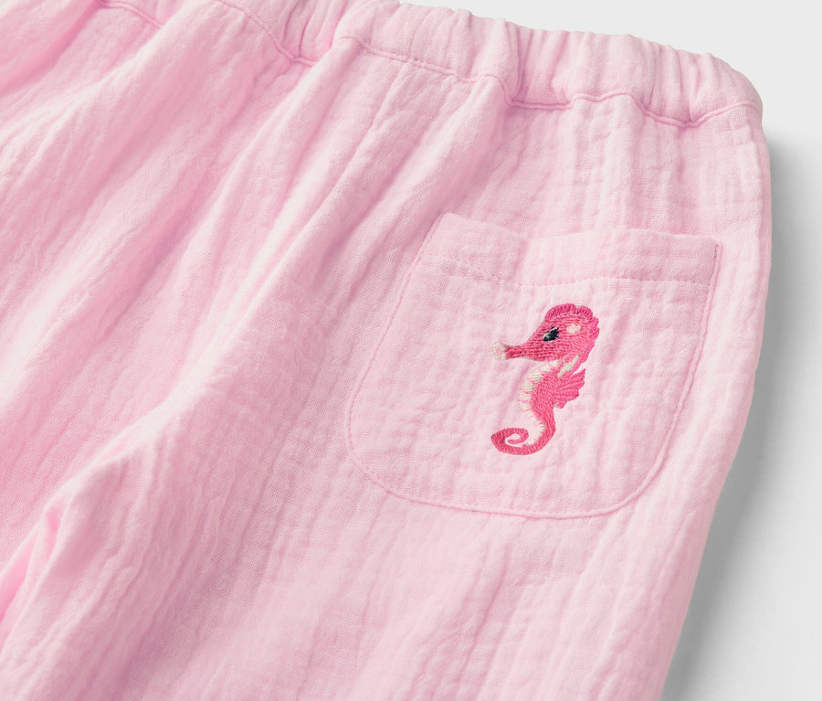 Gros plan d'un pantalon rose avec une taille élastique et une poche plaquée ornée d'un hippocampe brodé.