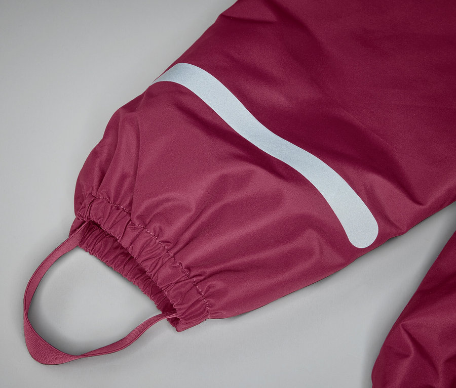 Gros plan sur une jambe de pantalon bordeaux avec ourlet élastique, boucle et bande réfléchissante sur fond gris.