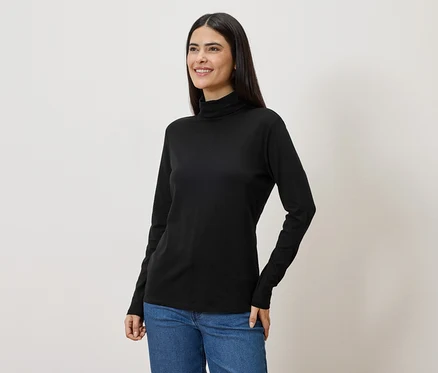 Une femme aux longs cheveux foncés porte un pull à col roulé noir et un jean.