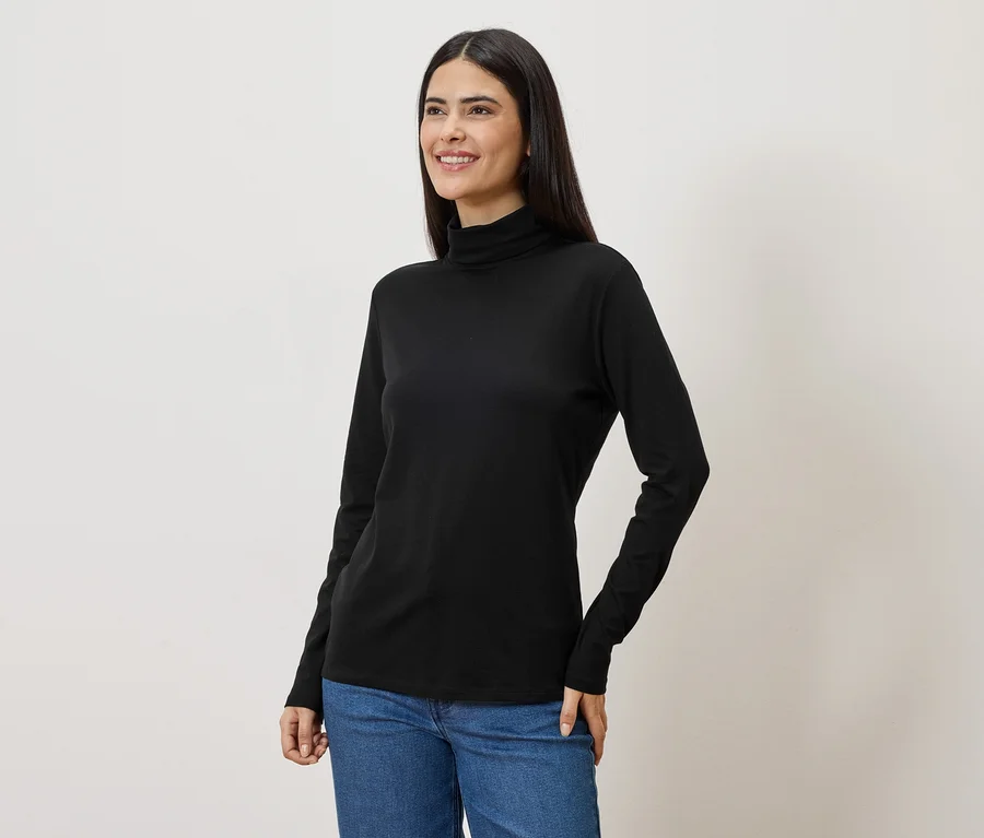 Une femme aux longs cheveux foncés porte un pull à col roulé noir et un jean.