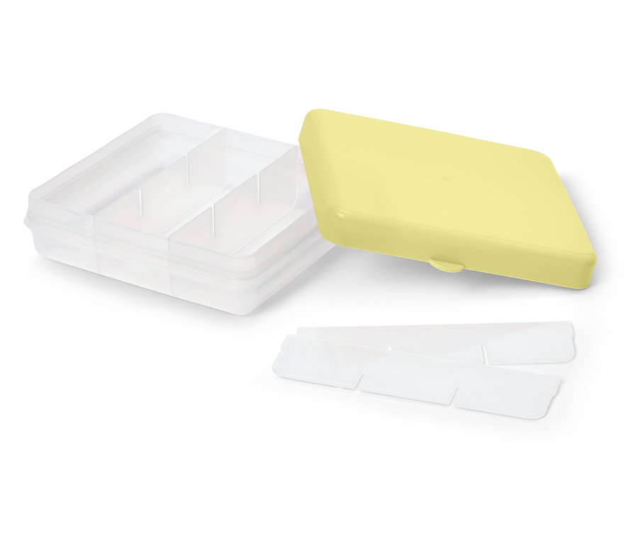 Une boîte de rangement transparente avec un couvercle jaune et des séparateurs repose sur un fond blanc.