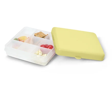 Boîte à lunch transparente ouverte avec un couvercle jaune. Remplie de bonbons, de crackers, de tomates et de fromage.