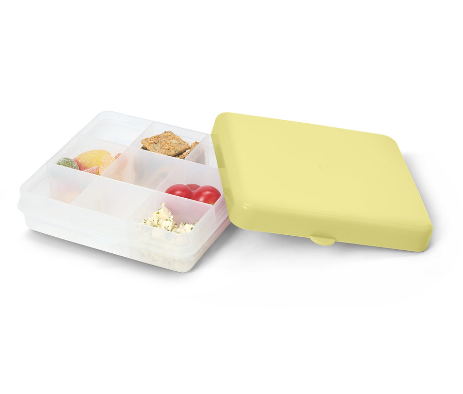 Boîte à lunch transparente ouverte avec un couvercle jaune. Remplie de bonbons, de crackers, de tomates et de fromage.