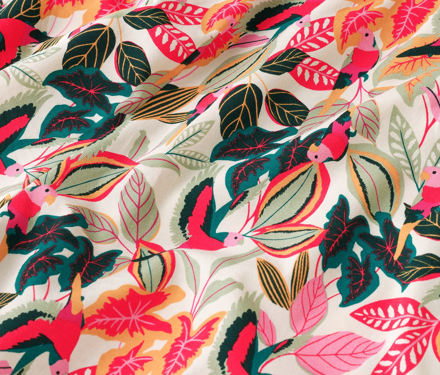 Gros plan d'un tissu à motifs d'oiseaux et de feuilles dans les tons rouge, vert et jaune.