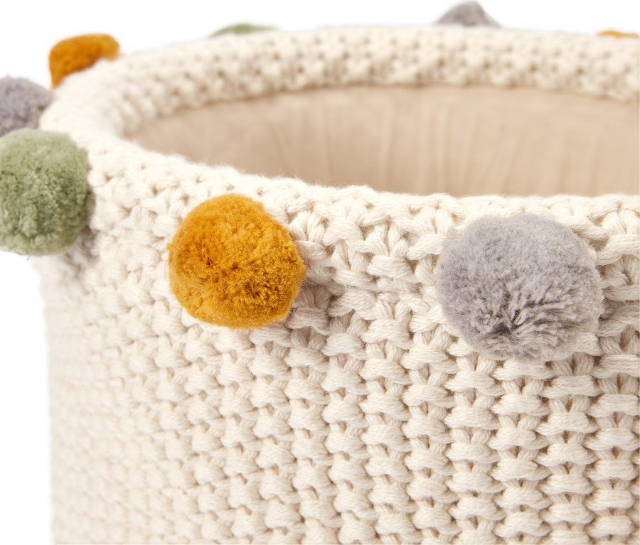 Gros plan d'un panier blanc tricoté avec des pompons colorés sur le bord.