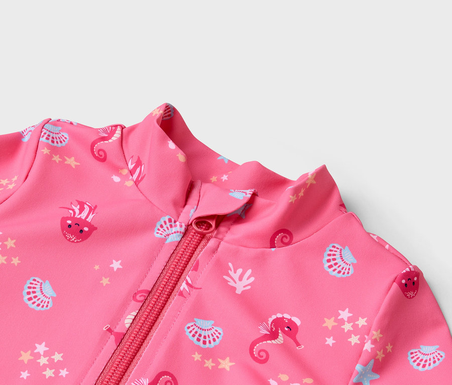 Gros plan sur un maillot de bain rose zippé avec des motifs d'hippocampes, de coquillages et d'étoiles.