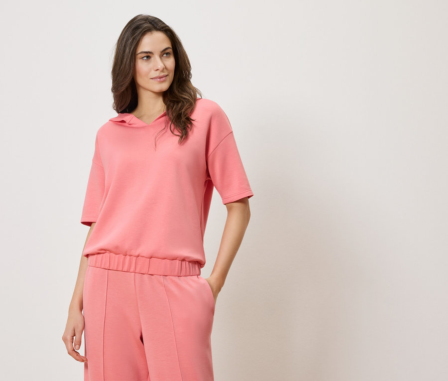 Femme portant un sweat à capuche rose à manches courtes et un pantalon rose.