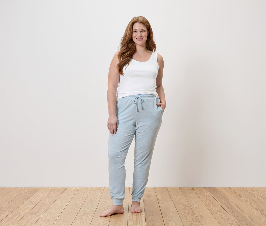Femme aux longs cheveux roux portant un débardeur blanc et un pantalon de jogging bleu clair.