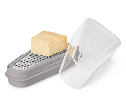 Un morceau de fromage est posé sur une râpe grise avec récipient et couvercle transparent.