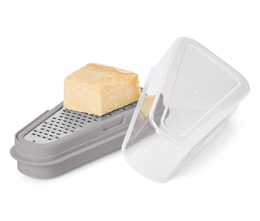 Un morceau de fromage est posé sur une râpe grise avec récipient et couvercle transparent.