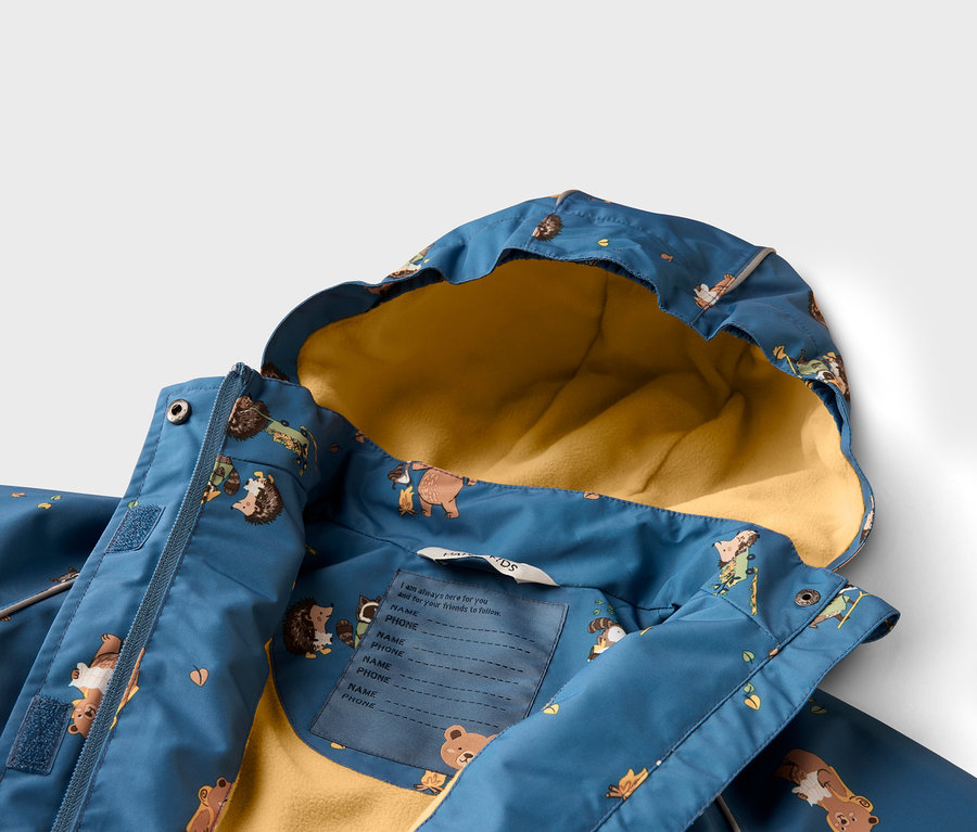 Gros plan d'un manteau pour enfant bleu avec une doublure jaune et un motif animalier. Une étiquette pour le nom et le numéro de téléphone est visible.