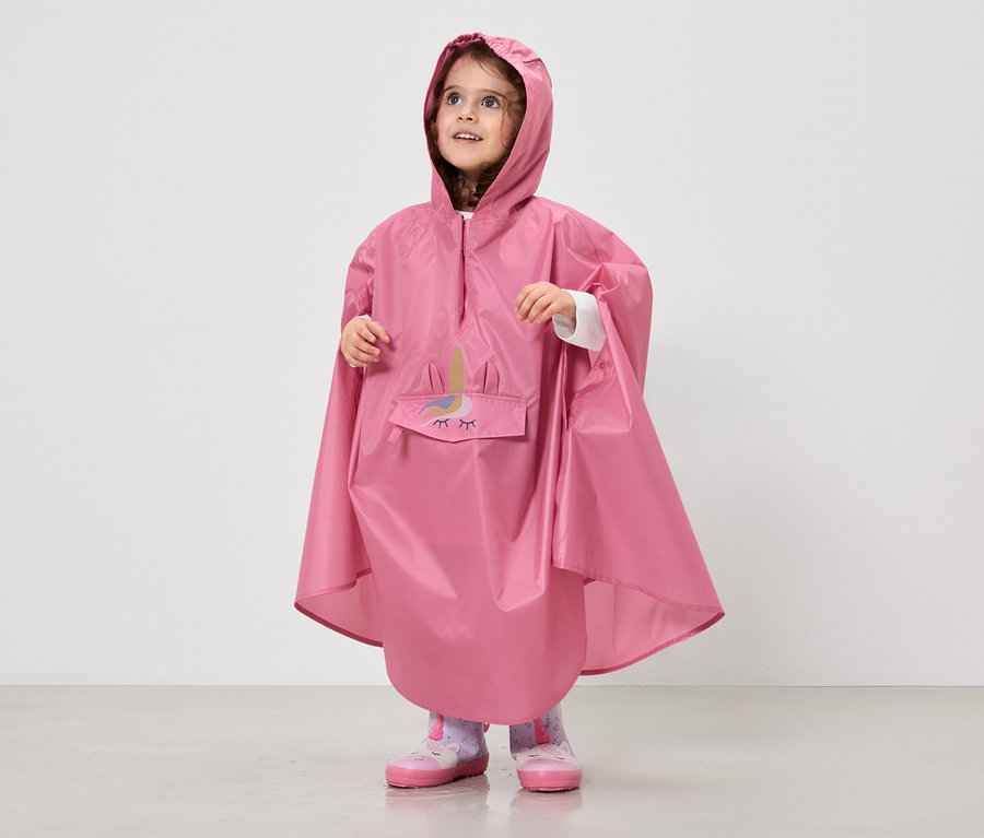 Une fillette porte un poncho de pluie rose à capuche avec un motif de licorne.