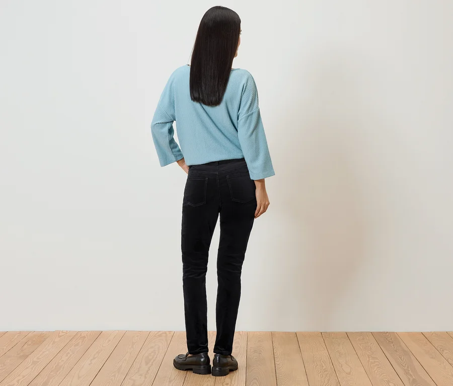 Une femme aux cheveux foncés, vue de dos, porte un haut bleu clair, un pantalon noir et des chaussures.