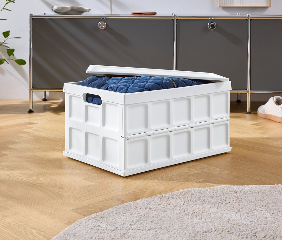Une boîte pliante blanche avec un contenu bleu est posée sur un plancher en bois devant une armoire grise et des chaussures.