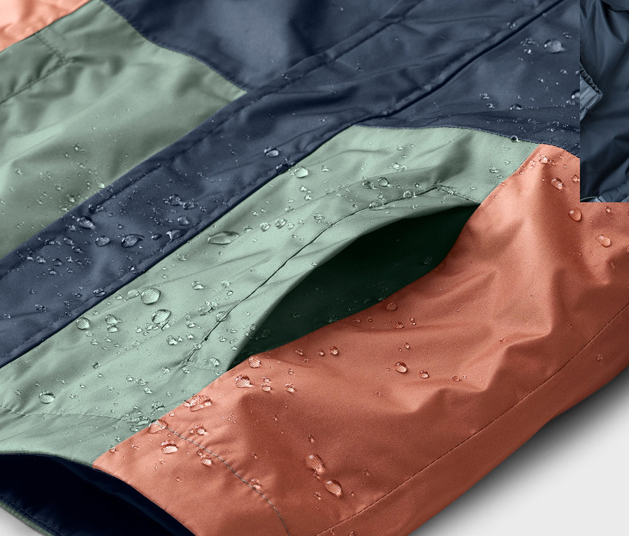 Gros plan sur une veste imperméable à blocs de couleurs bleu, vert et orange avec des gouttes d'eau et une poche.