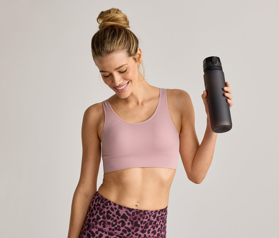 Femme souriante en brassière de sport et legging tenant une bouteille d'eau noire.