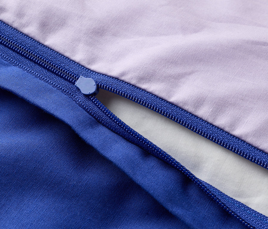 Gros plan sur une fermeture éclair partiellement ouverte sur un tissu violet et bleu.