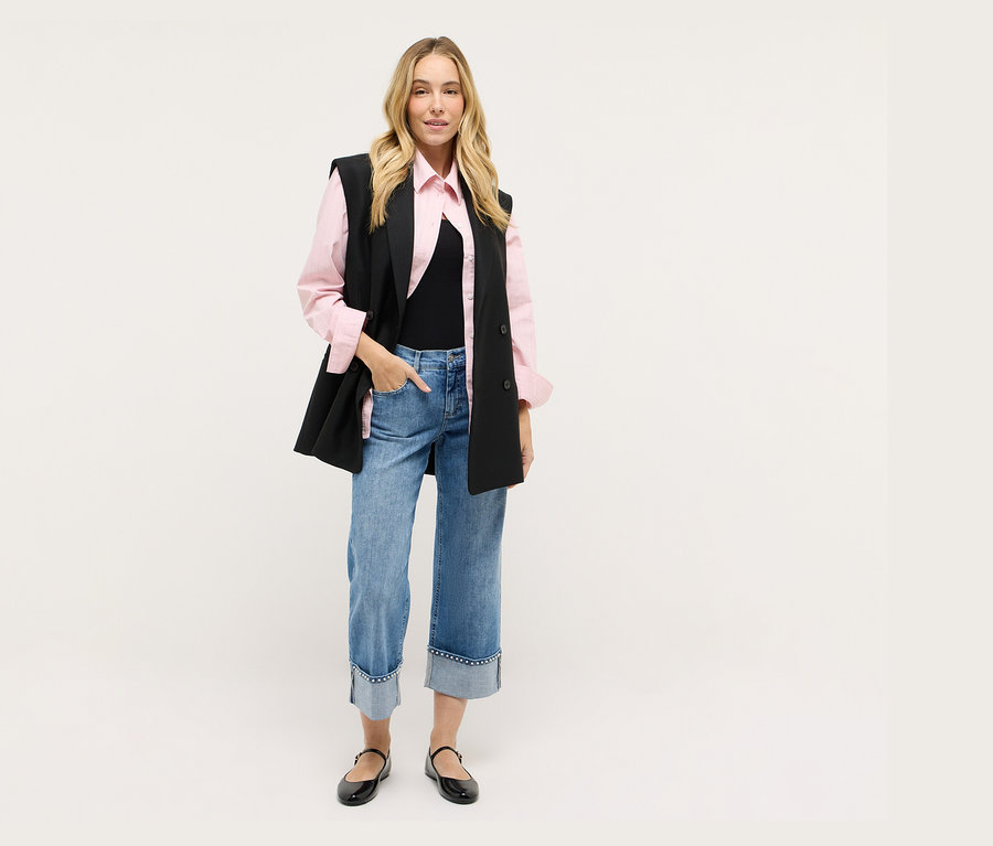 Femme portant un gilet noir, une chemise rose, un jean et des chaussures noires.