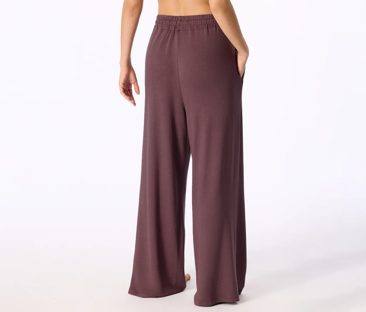 Personne de dos portant un pantalon large marron foncé avec une taille élastique et une main dans la poche, le haut du dos est visible.