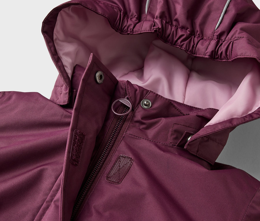 Veste bordeaux avec capuche, fermeture éclair et boutons-pression. La capuche a une doublure rose clair et une bande réfléchissante.