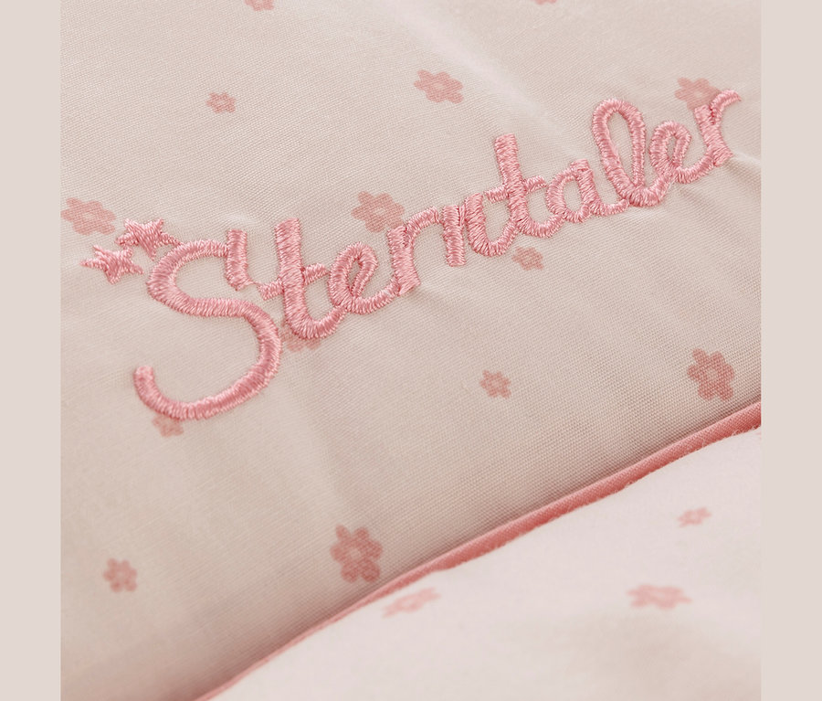 Gros plan d'un tissu rose clair avec un motif floral délicat et le lettrage brodé « Sterntaler » en rose plus foncé.
