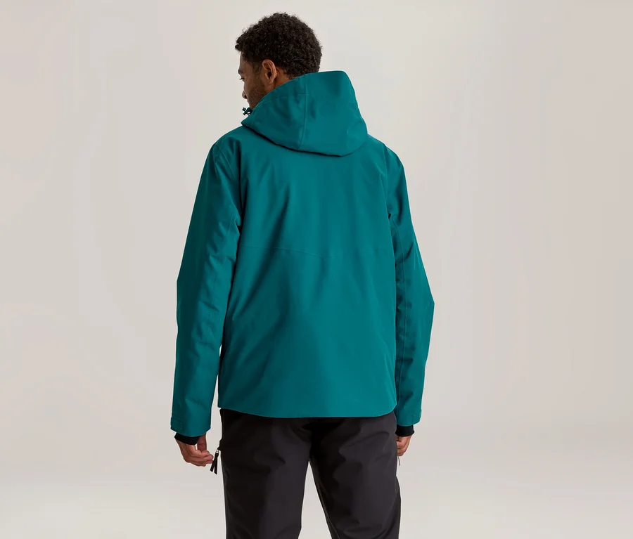 Homme de dos, portant une veste à capuche turquoise et un pantalon noir, regardant légèrement vers la droite.