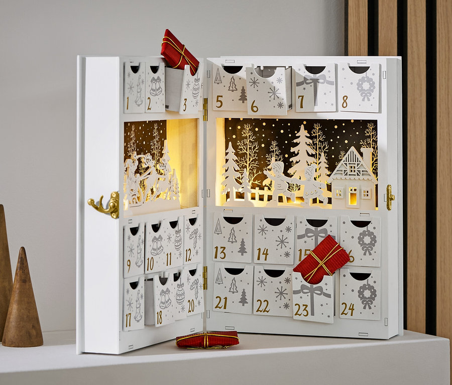 Calendrier de l'Avent blanc ouvert avec décorations et cadeaux, à côté de trois cônes en bois.