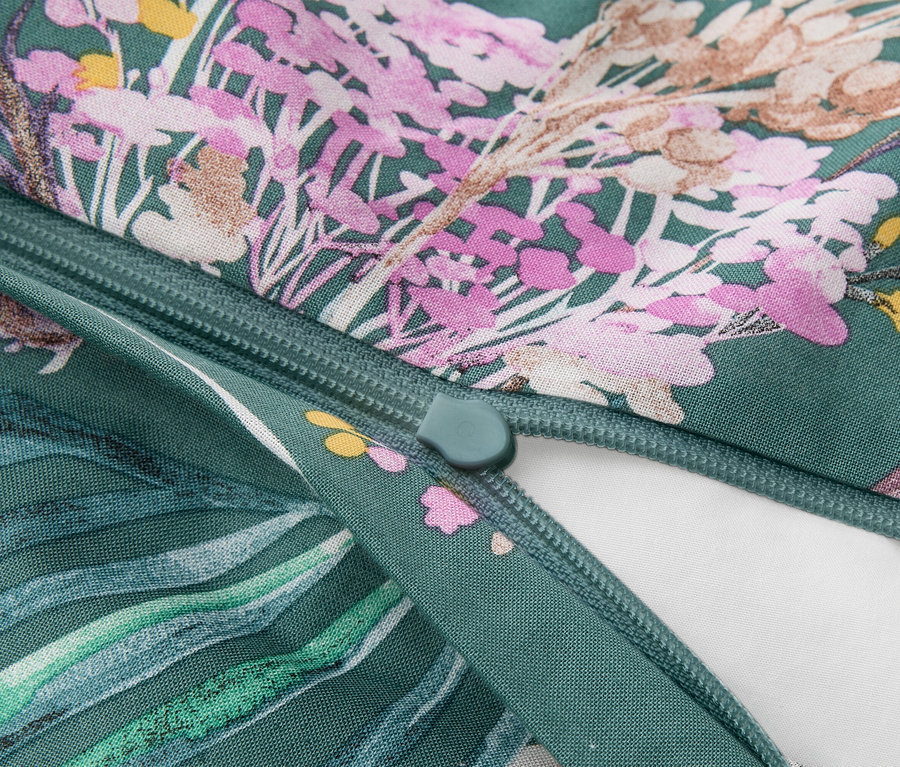 Gros plan d'un tissu vert à motif floral rose, violet, jaune et marron, avec une fermeture éclair verte partiellement ouverte révélant une doublure blanche.