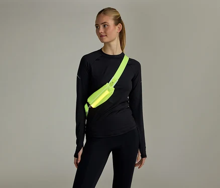 Femme aux cheveux attachés, vêtue d'un haut noir à manches longues et d'un legging noir, portant un sac banane jaune fluo en bandoulière.