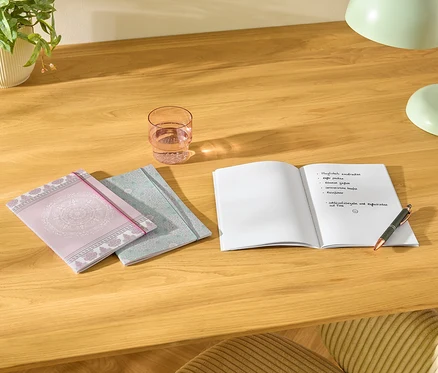 Sur une table, il y a trois carnets, un verre d'eau, un carnet ouvert avec des notes et un stylo.