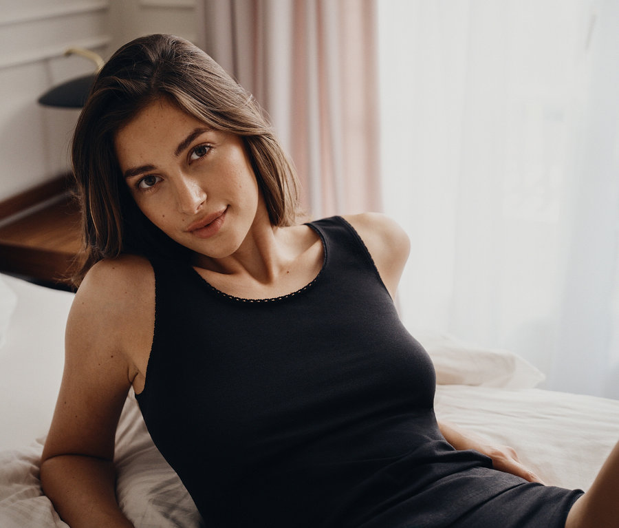 Portrait d'une femme allongée sur un lit portant un débardeur noir.