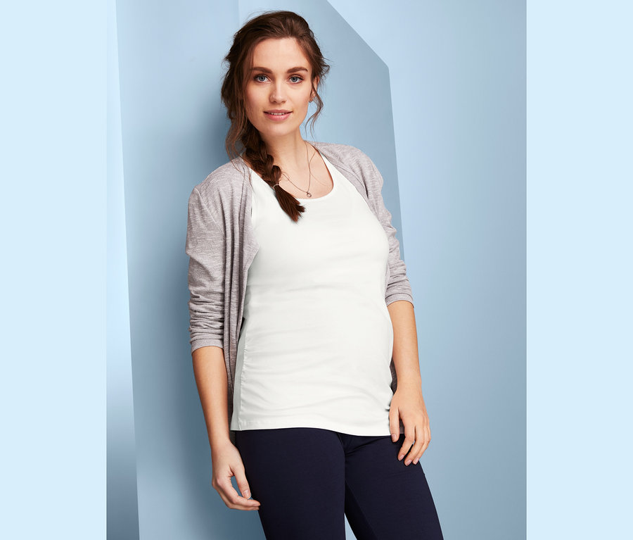 Femme enceinte posant dans un top blanc d'un lot de 2 hauts de grossesse et un cardigan gris.