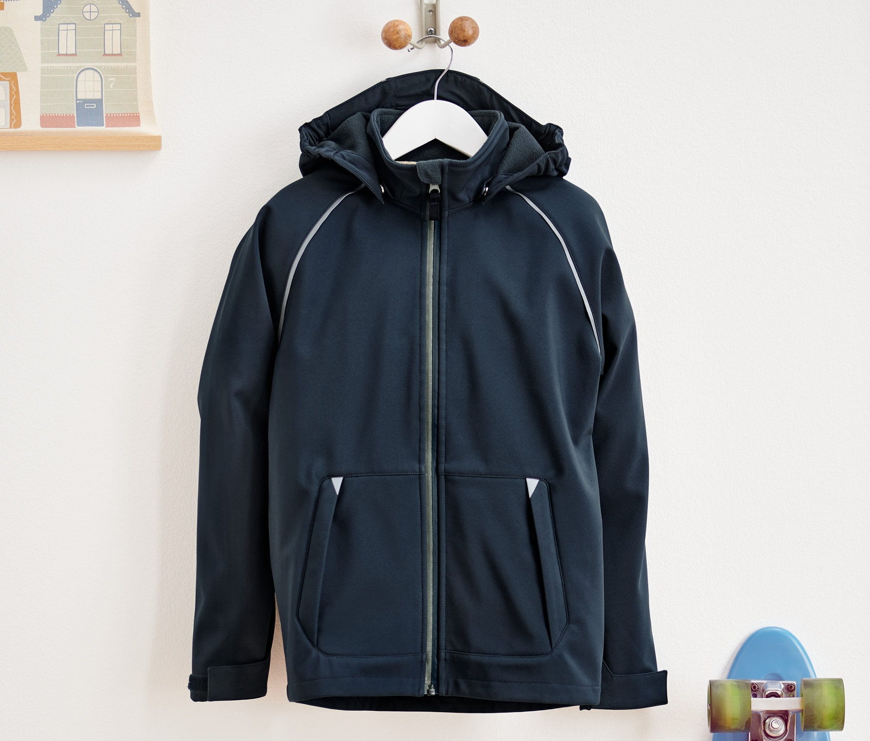 Une veste softshell bleu marine est suspendue à un cintre à côté d'une planche à roulettes bleue.