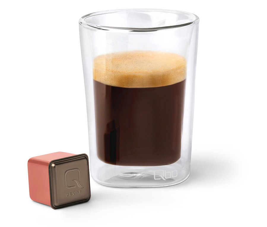 Une capsule Qbo Caffè MENOS CAFEÍNA à côté d'un verre de café.