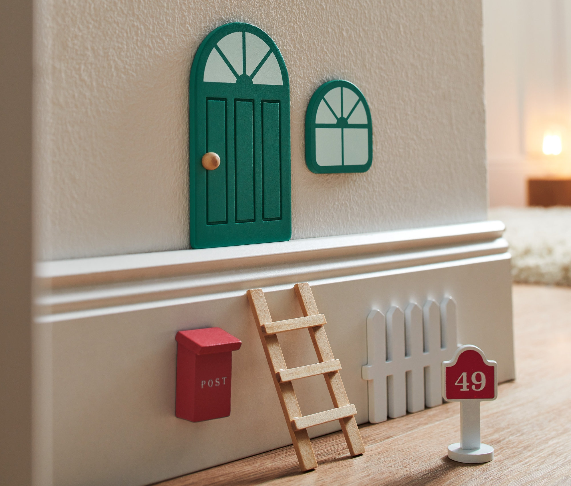 Un Kit porte de lutin comprenant une porte verte fermée, une fenêtre, une boîte aux lettres rouge, une échelle et une clôture blanche avec le numéro de maison 49.