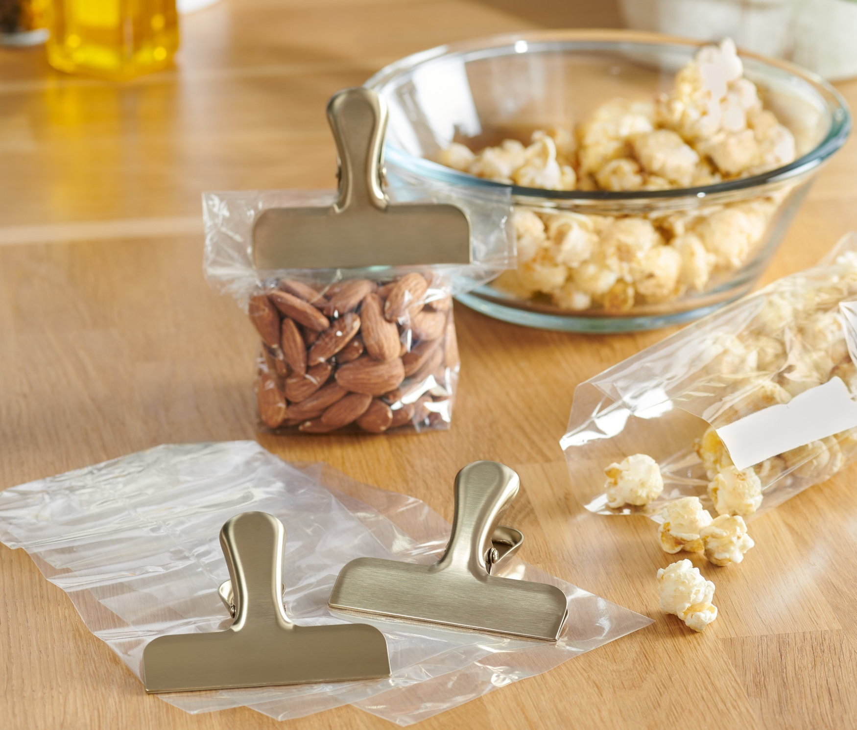 Sur une table en bois se trouvent 3 clips aromatiques en acier inoxydable, dont deux sur des sacs vides et un sur un sac d'amandes.