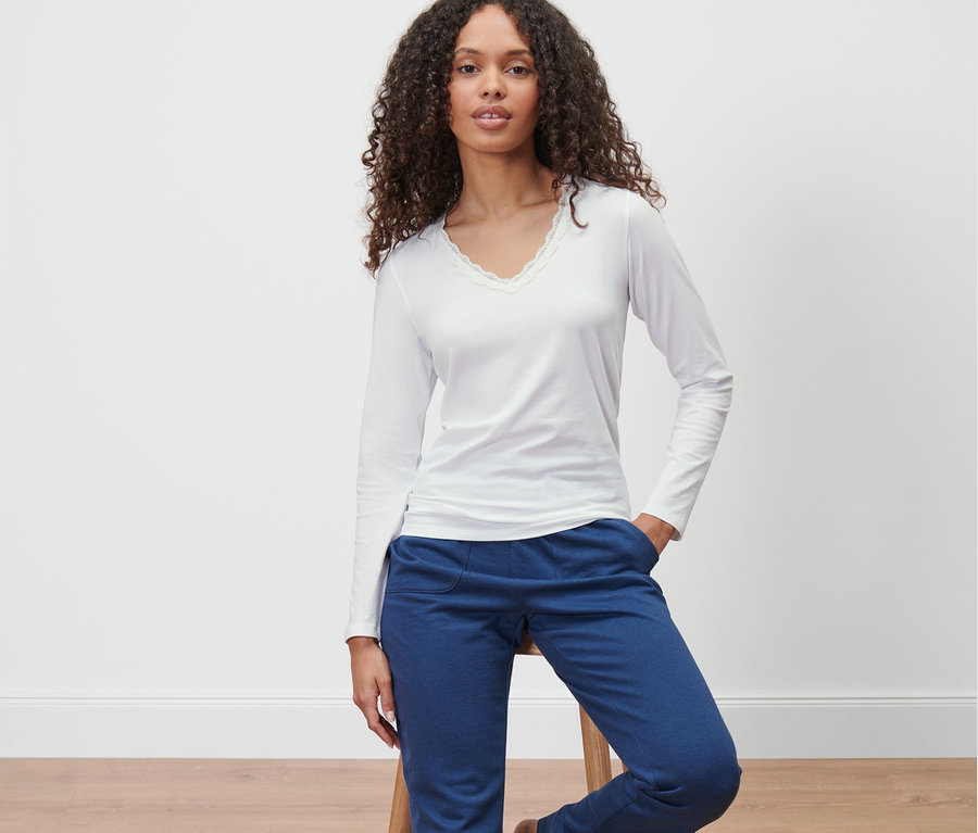 Femme assise sur un tabouret portant un maillot de corps manches longues et un pantalon bleu.